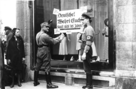 **A Nazi officer affixing a sign which tells shoppers to stop supporting a Jewish store**