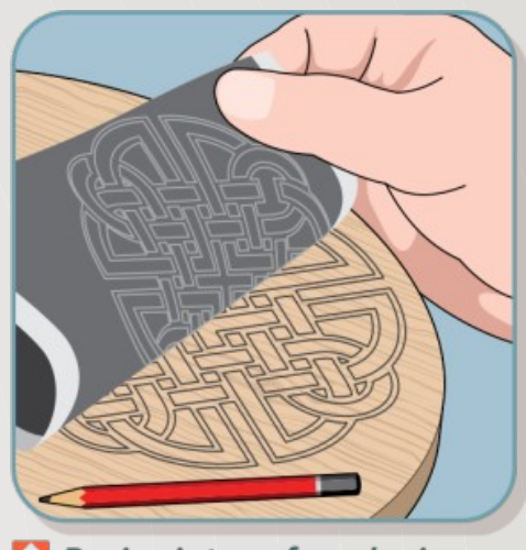 This image depicts a hand transferring a decorative design from a stencil onto a wooden surface. The design features an intricate Celtic knot pattern. A pencil lies nearby on the wood, suggesting the design is being traced or etched onto the wood.